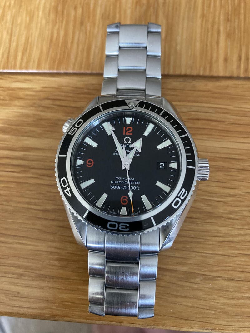 Omega Seamaster Planet Ocean 2201.51.00 Black Dial watch which was sold via Chrono Hunter displayed on beach colour wood 